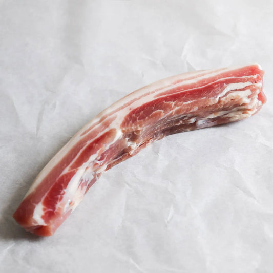 Thin slices of outdoor-reared, dry-cured unsmoked streaky bacon from Primrose Herd, showcasing marbled meat with a rich, natural color.