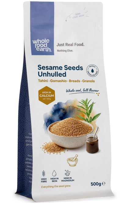 Unhulled sesame seeds in a clear bowl, showing small beige seeds with rough shells from Whole Food Earth, in natural lighting.