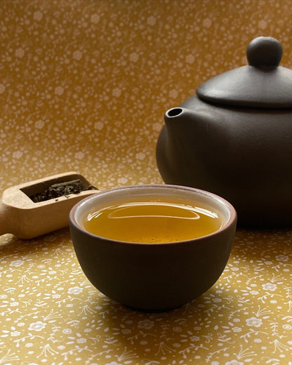 Porter Hill Tea Company hojicha green tea in a cozy tea cup with loose tea leaves on a wooden surface.