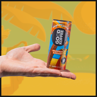A can of GOOD KOFFEE sparkling coffee with grapefruit and orange flavor, held in a person's hand against a background with palm leaves and yellow and orange colors.
