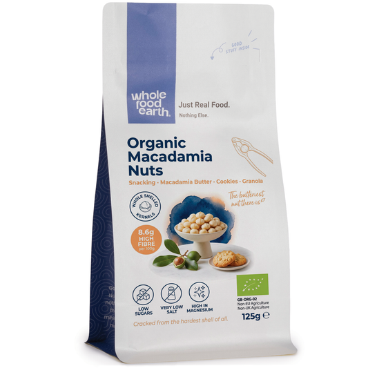Raw organic macadamia nuts from Whole Food Earth, whole and shelled, in a bowl on a wooden surface.