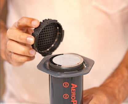 Stainless steel filter for AeroPress coffee maker by Contact Coffee Company Ltd., shown with the filter and AeroPress gear.