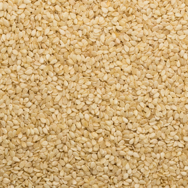 Unhulled sesame seeds in a clear bowl, showing small, tan seeds with textured shells, on a white background.