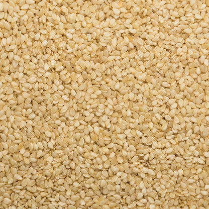 Unhulled sesame seeds in a clear bowl, showing small, tan seeds with textured shells, on a white background.