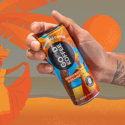 A hand holding a can of GOOD KOFFEE Sparkling Coffee in Grapefruit & Orange flavor, set against a stylized orange and gray background with tropical leaf silhouettes.