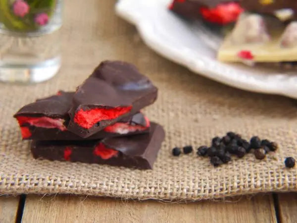 Handmade Gorvett & Stone dark chocolate shards with berry and pepper flavors, displayed on a rustic wooden surface.