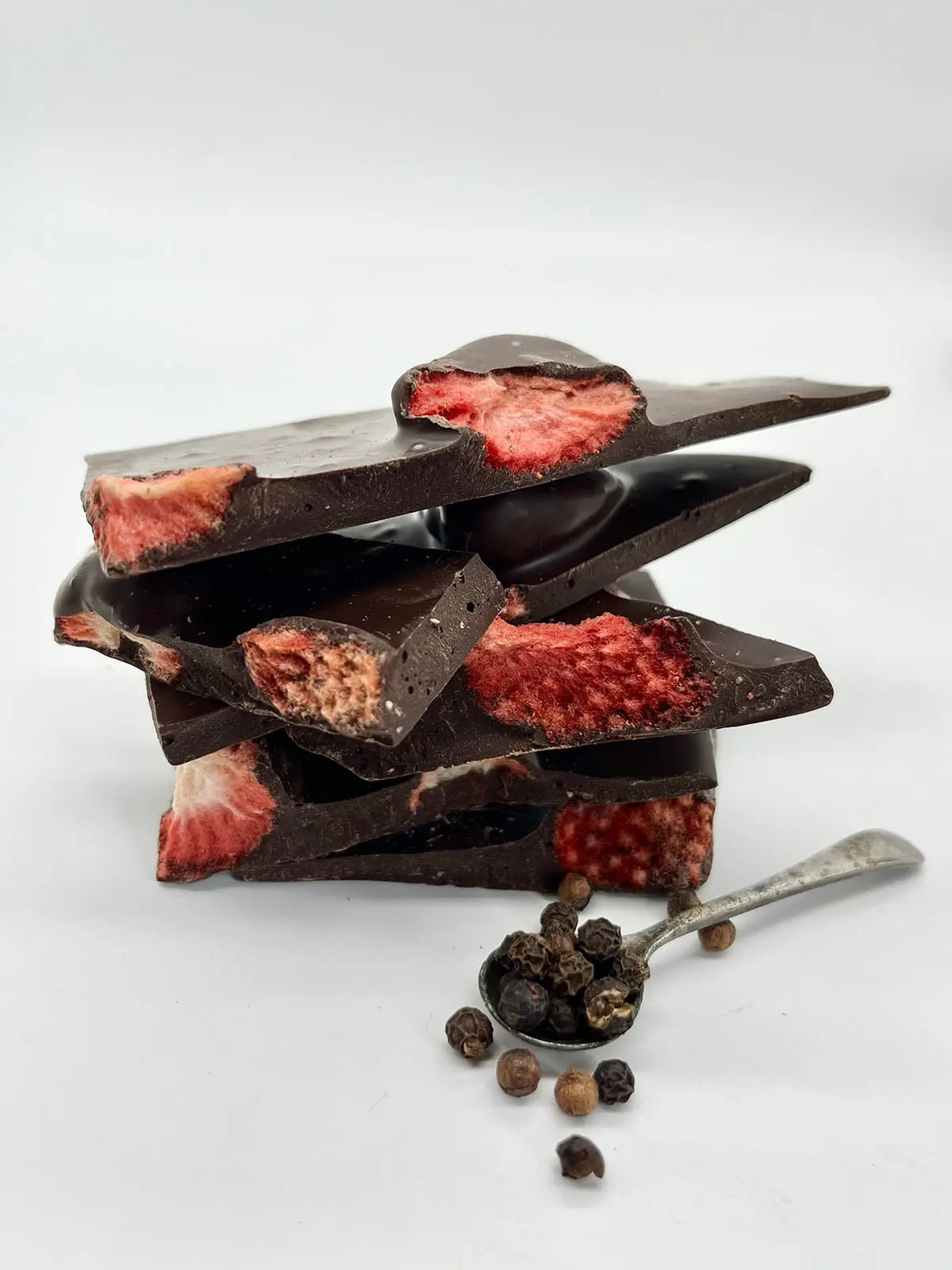 Handmade Gorvett & Stone berry peppery dark chocolate shards on a rustic surface, showcasing rich, textured chocolate pieces.