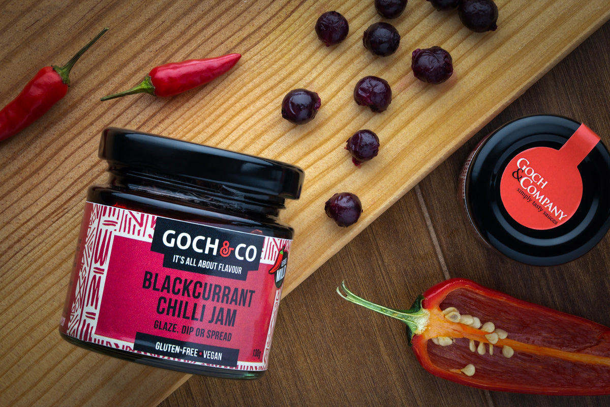 Blackcurrant chilli jam in a jar with blackcurrants and red chilli peppers, produced by Goch & Co.