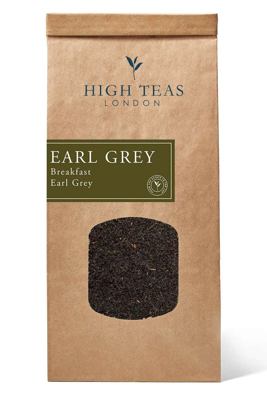 A box of High Teas Breakfast Earl Grey tea with loose tea leaves and a teacup on a wooden table.