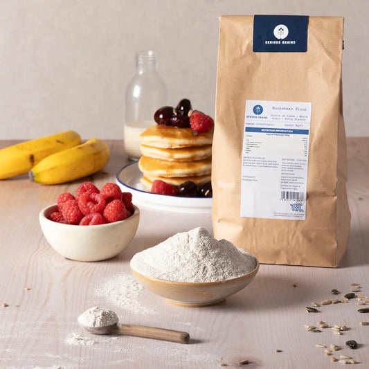 Organic buckwheat flour in a bag, shown on a rustic kitchen counter with baking ingredients and wooden spoons for a natural baking scene.