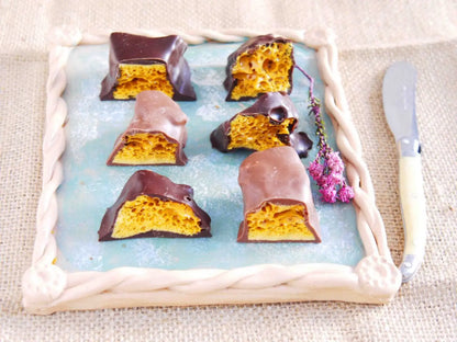 Handmade cinder toffee covered in 70% dark chocolate, displayed with honeycomb pieces in a natural setting.