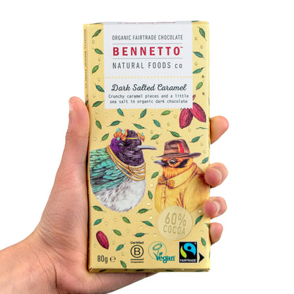 Hand holding Bennetto Natural Foods UK dark salted caramel chocolate bar, showcasing rich, textured chocolate with caramel filling.