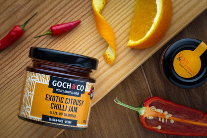 Glass jar of Goch & Co Exotic Citrusy Chilli Jam showing vibrant orange chili and citrus chunks inside.
