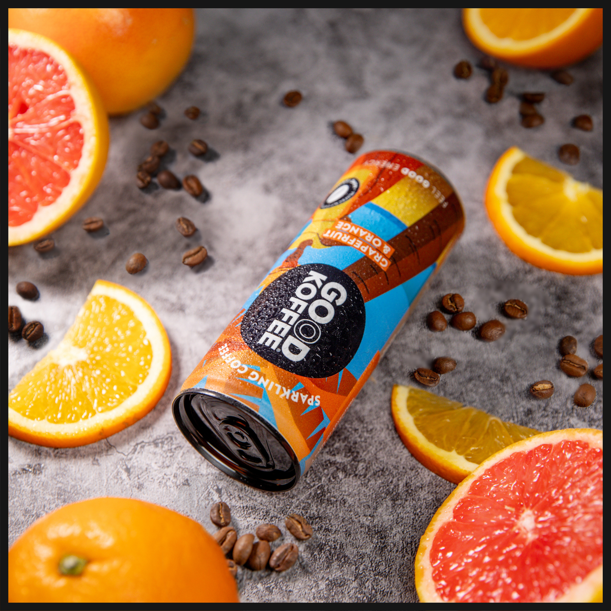 GOOD KOFFEE Barbados Grapefruit & Orange sparkling coffee 12-pack on a grey background surrounded by coffee beans and slices of orange and grapefruit.