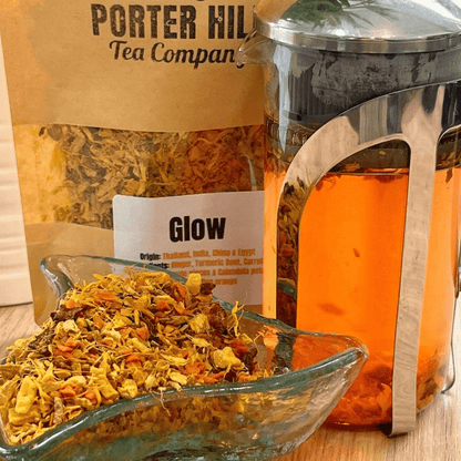 Porter Hill Tea Company's Glow fruit and herbal tea in a clear glass cup with fresh herbs and fruit slices for a vibrant, refreshing look.