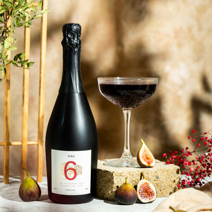 Bottle of Turn 6 premium alcohol-free sparkling red wine with a dark label and elegant glass, showcasing the product's rich color.