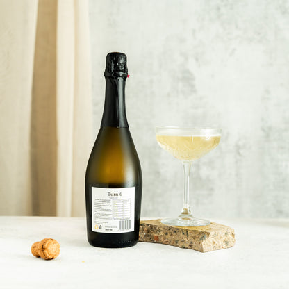 Six bottles of Turn 6 premium alcohol-free sparkling white wine in a case, showcasing clear glass bottles and elegant labels.