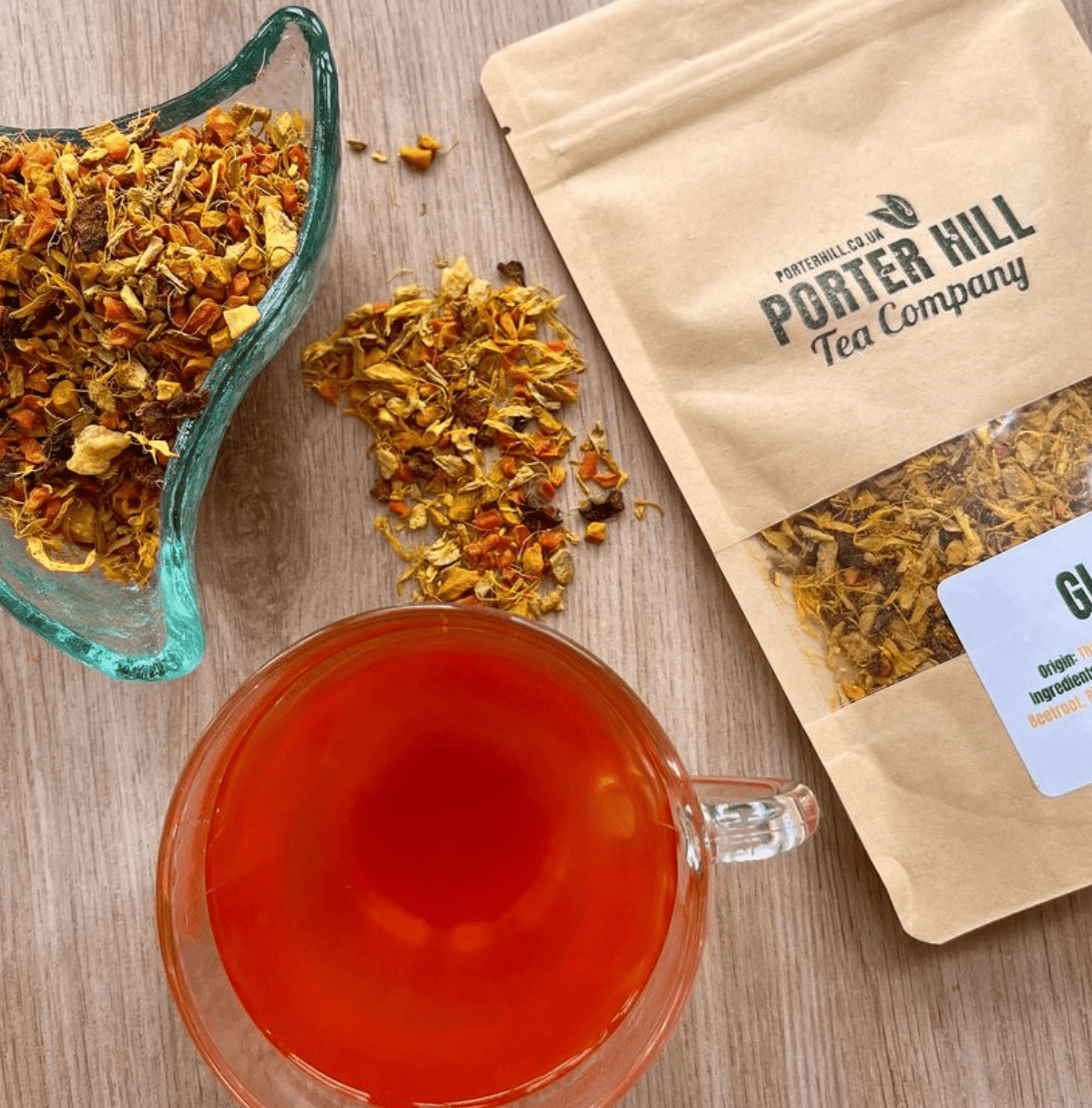 Porter Hill Tea Company's Glow fruit and herbal tea in a clear glass cup with vibrant tea infusion and fresh herbs.