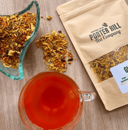 Porter Hill Tea Company's Glow fruit and herbal tea in a clear glass cup with vibrant tea infusion and fresh herbs.