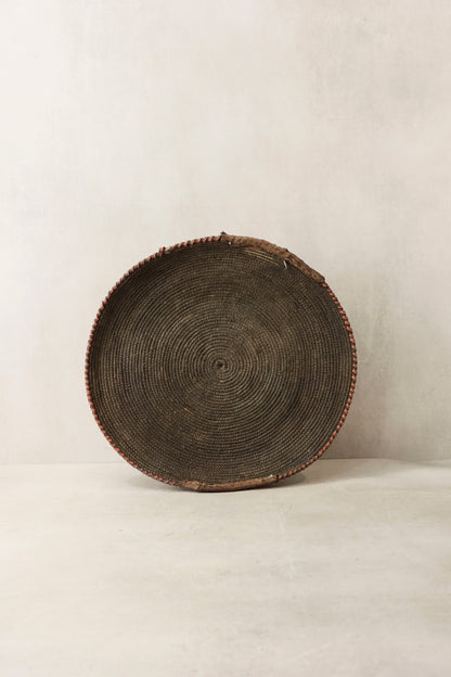 Handwoven wall basket from Chad by Botanical Boys, made of natural fibers, displayed hanging on a wall.