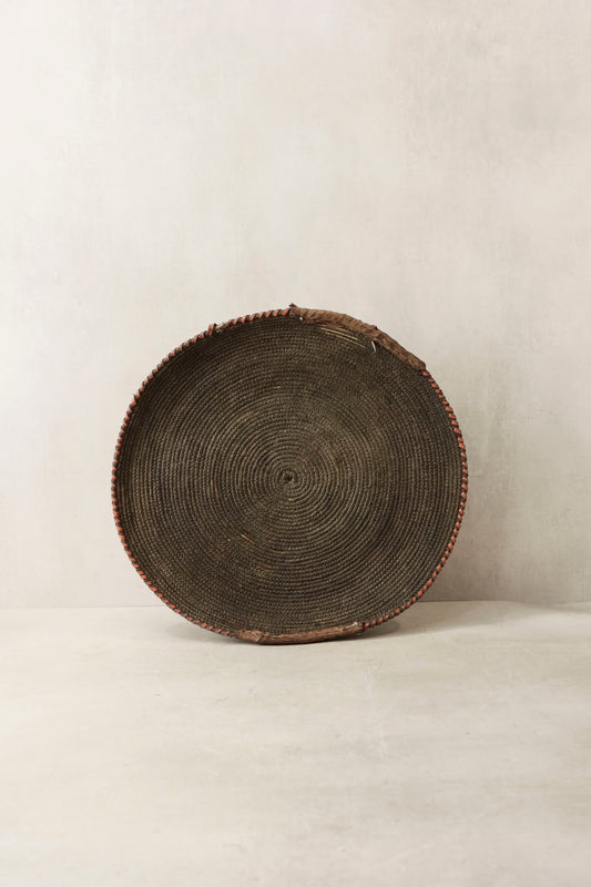 Handwoven wall basket from Chad by Botanical Boys, made of natural fibers, displayed hanging on a wall.