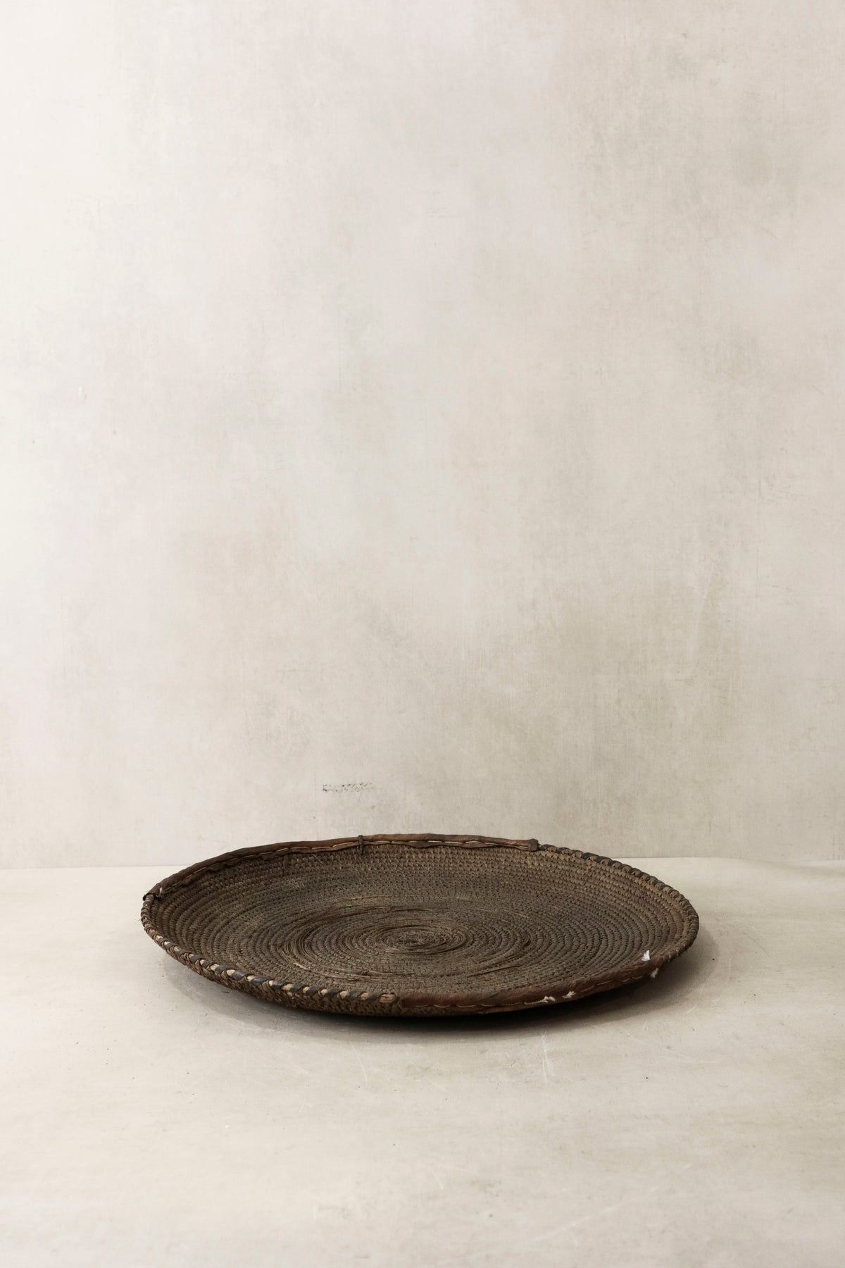 Handwoven wall basket from Chad by Botanical Boys, made of natural fibers, hanging on a wall for decorative storage.