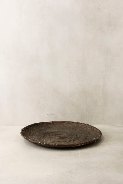 Handwoven wall basket from Chad by Botanical Boys, made of natural fibers, hanging on a wall for decorative storage.