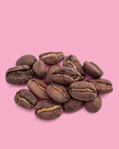 Spilled Colombia Finca Maracay medium roast coffee beans from Recent Beans on a pink surface.