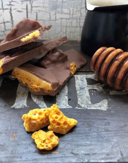 Creamy milk chocolate honeycomb shards from Gorvett & Stone, displayed in a natural, rustic setting with broken chocolate pieces.
