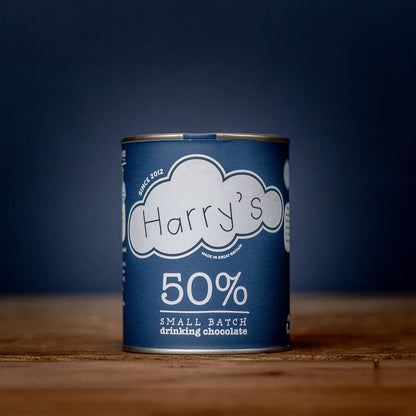A cup of Harry's Hot Chocolate with 50% hot chocolate mix, topped with whipped cream and cocoa powder on a cozy table.