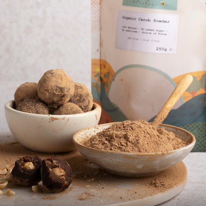 Organic carob powder in a jar, with a spoon and bowls of ingredients, displayed in a natural lifestyle setting.