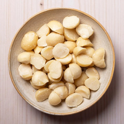 Organic macadamia nuts from Whole Food Earth, shown in a bowl with some nuts and shells on a wooden surface.