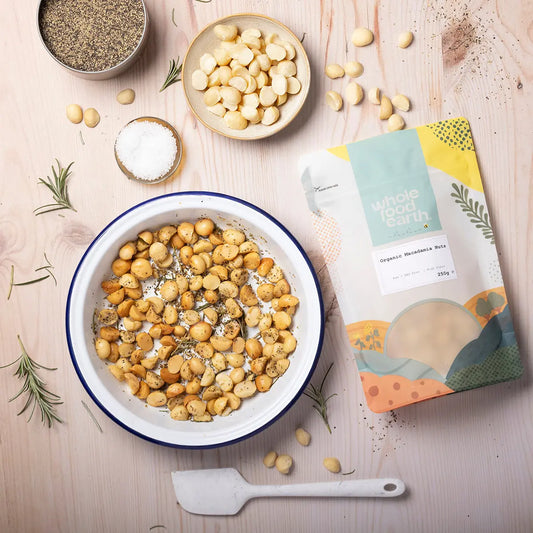 Organic macadamia nuts from Whole Food Earth, displayed in a natural setting with nuts and shells on a wooden surface.