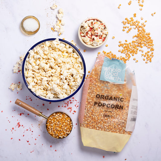 Organic popcorn in a bowl, displayed on a rustic wooden table, with whole grains and popcorn kernels visible.