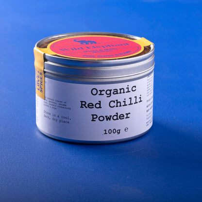 Organic red chili powder from Whole Food Earth, a vibrant 100g herbs and spices container showing bright red chili powder inside.