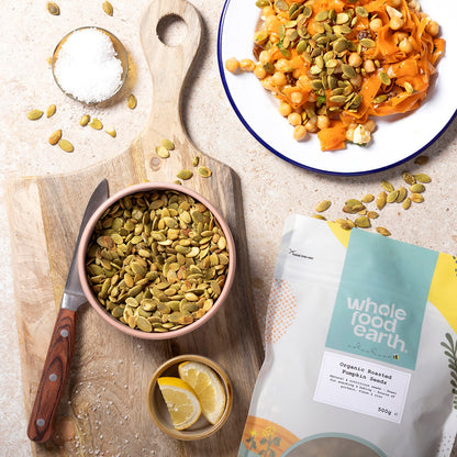 Organic roasted pumpkin seeds from Whole Food Earth, displayed in a bowl with fresh pumpkin in the background.