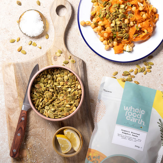 Organic roasted pumpkin seeds from Whole Food Earth, displayed in a bowl with fresh pumpkin in the background.