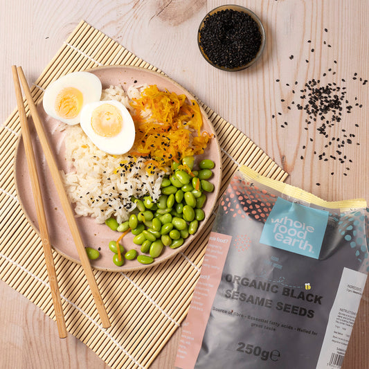 Black organic sesame seeds from Whole Food Earth, shown in a bowl with some seeds scattered on a wooden surface.