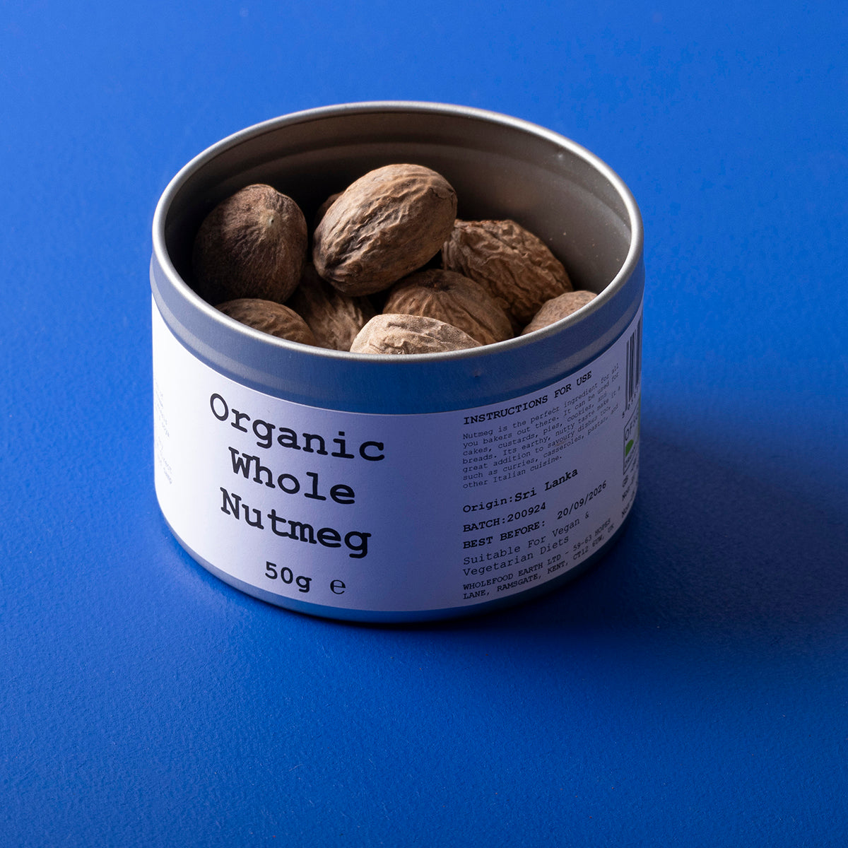 Whole Food Earth organic whole nutmeg in a clear container, showing whole, brown spice with textured surface.