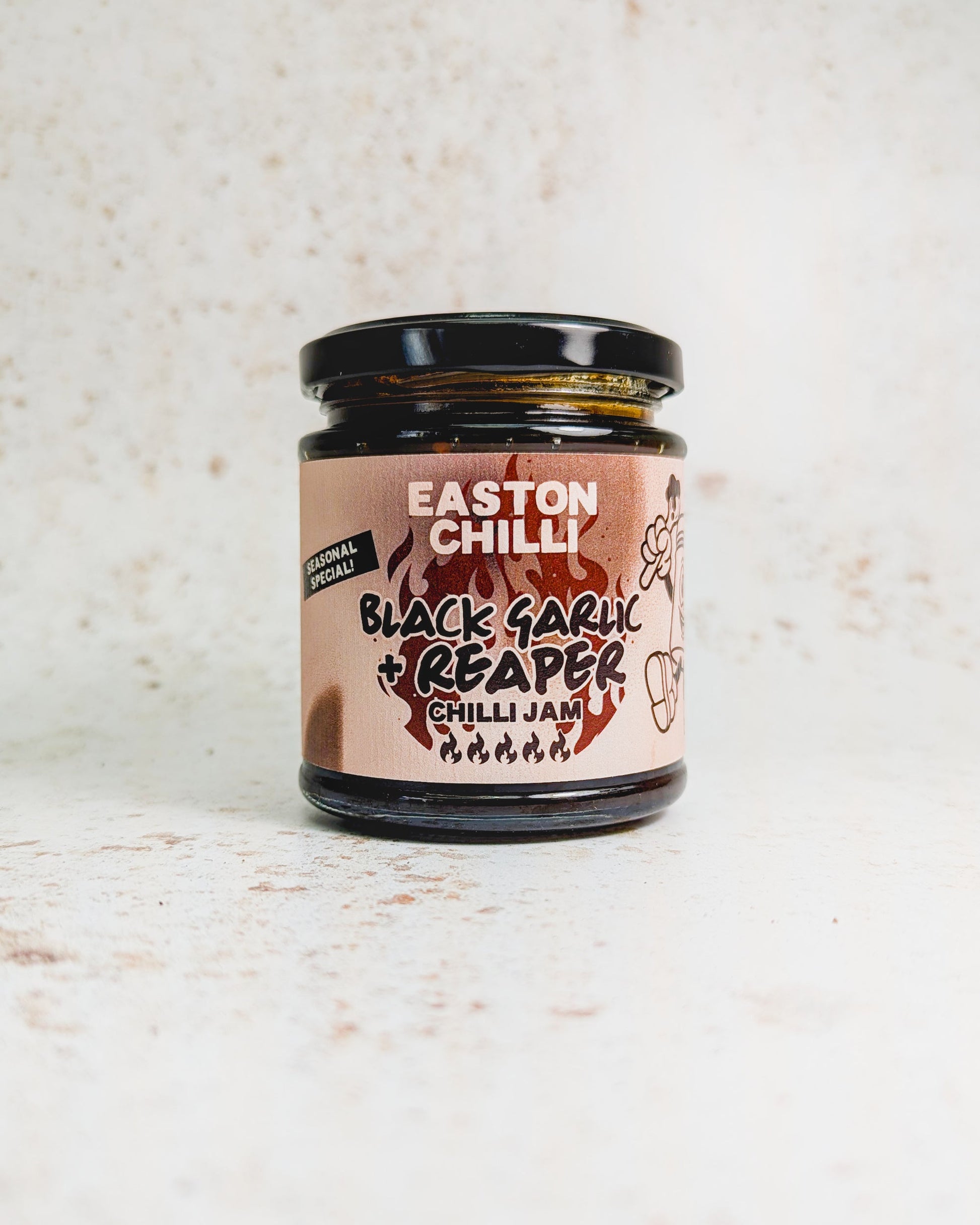 Black garlic and Reaper chili jam by Easton Chilli, shown in a jar with black garlic cloves and vibrant chili peppers.
