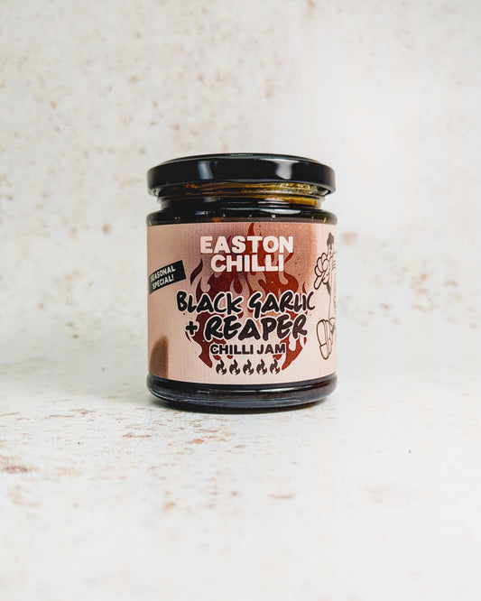 Black garlic and Reaper chili jam by Easton Chilli, shown in a jar with black garlic cloves and vibrant chili peppers.