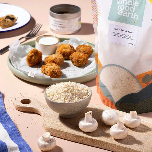 Whole Food Earth Panko Breadcrumbs in a bowl, perfect for cooking and baking, with a spoon and scattered crumbs on a wooden table.