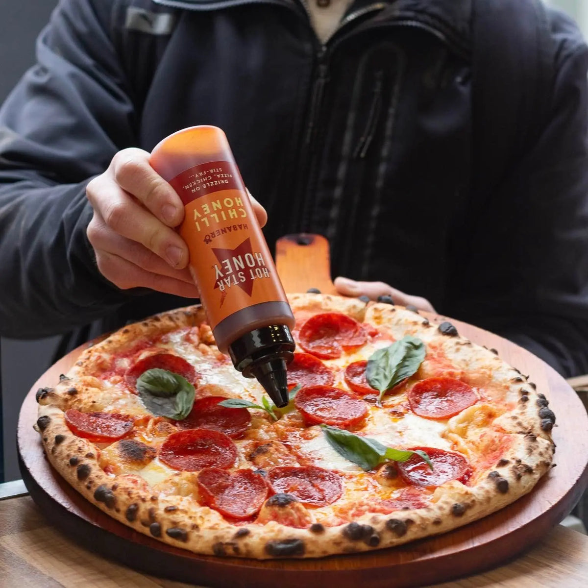 Habanero hot chili honey from Hot Star Honey drizzled on a pizza, showing vibrant red habanero peppers and golden honey.