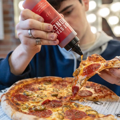 Scotch Bonnet chilli honey by Hot Star Honey drizzled on a pizza, showcasing the spicy-sweet glaze and vibrant chili peppers.