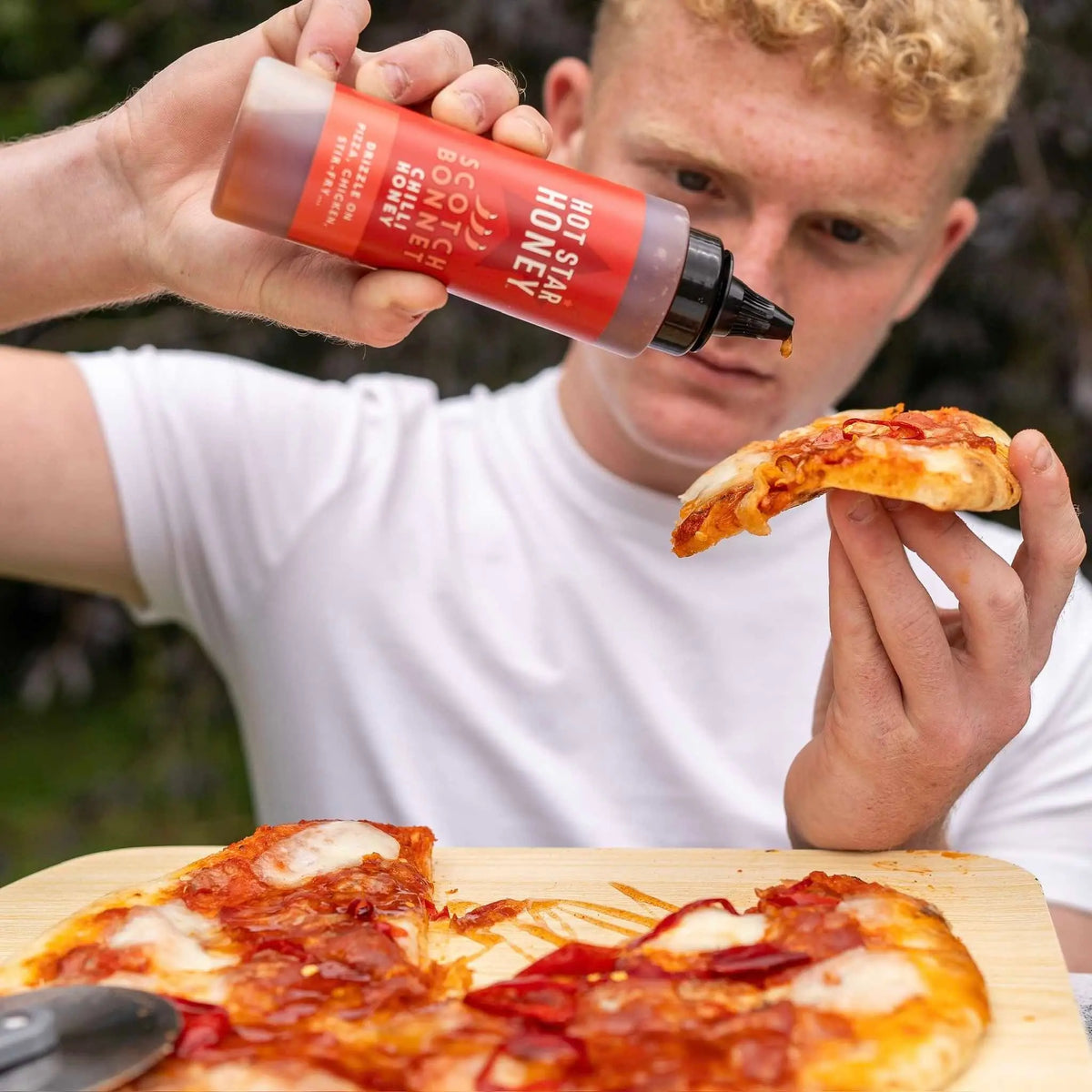 Hot Star Honey chilli honey set with a jar of spicy honey and a slice of pizza topped with chili honey and herbs.