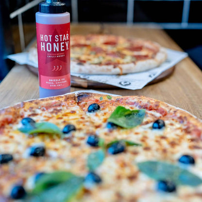 Scotch bonnet chilli honey from Hot Star Honey drizzled on pizza, showcasing vibrant chilli peppers and golden honey.