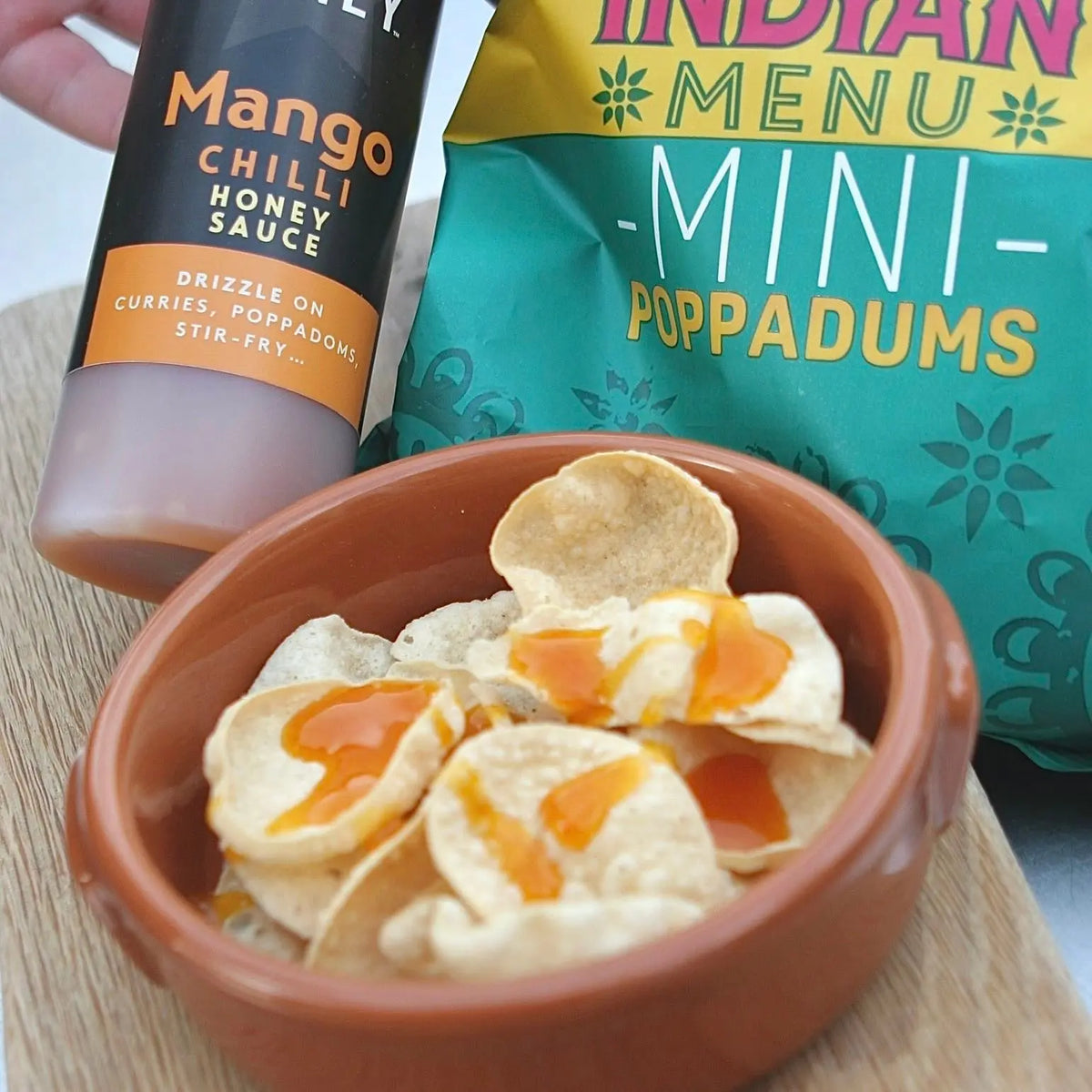 Sweet and spicy mango chili honey sauce drizzled over crispy popadoms, showcasing Asian-inspired flavors from Hot Star Honey.