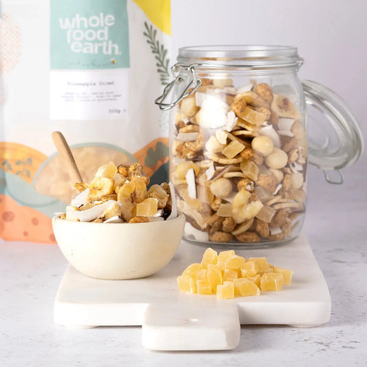 Dried pineapple diced pieces in a clear bowl, showcasing the Whole Food Earth dried fruits product on a rustic wooden surface.