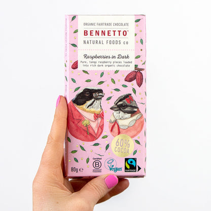 Hand holding dark chocolate with fresh raspberries from Bennetto Natural Foods UK, showcasing the rich chocolate and vibrant berries.