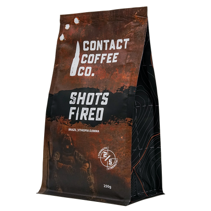 A bag of Shots Fired Coffee by Contact Coffee Company Ltd. with a bold label featuring the Shots Fired logo and vibrant design.